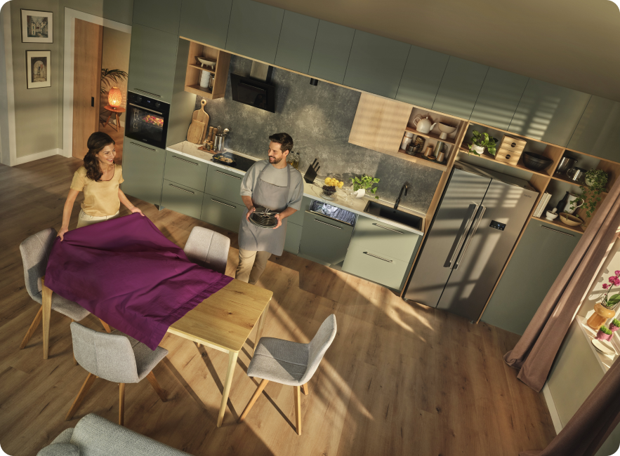 femeie aranjeaza masa si barbat aducand vase, bucatarie moderna